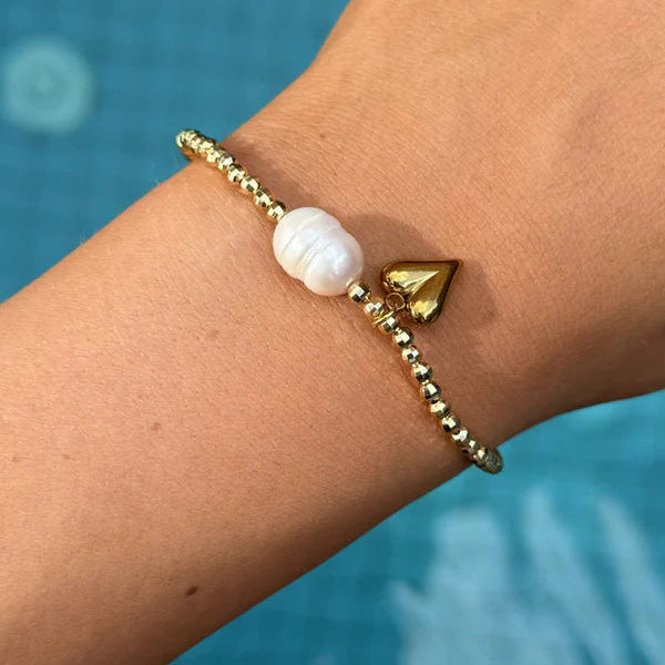 Gold bracelet with a white bead on a wrist against a blue water background