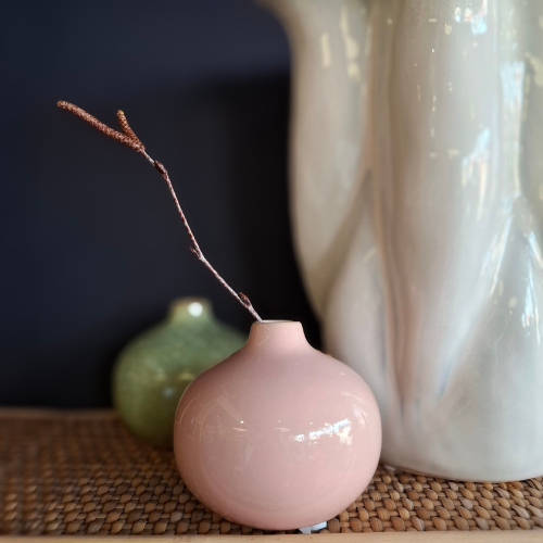 Pink ceramic bud vase with a twig on a textured surface with a blurred background