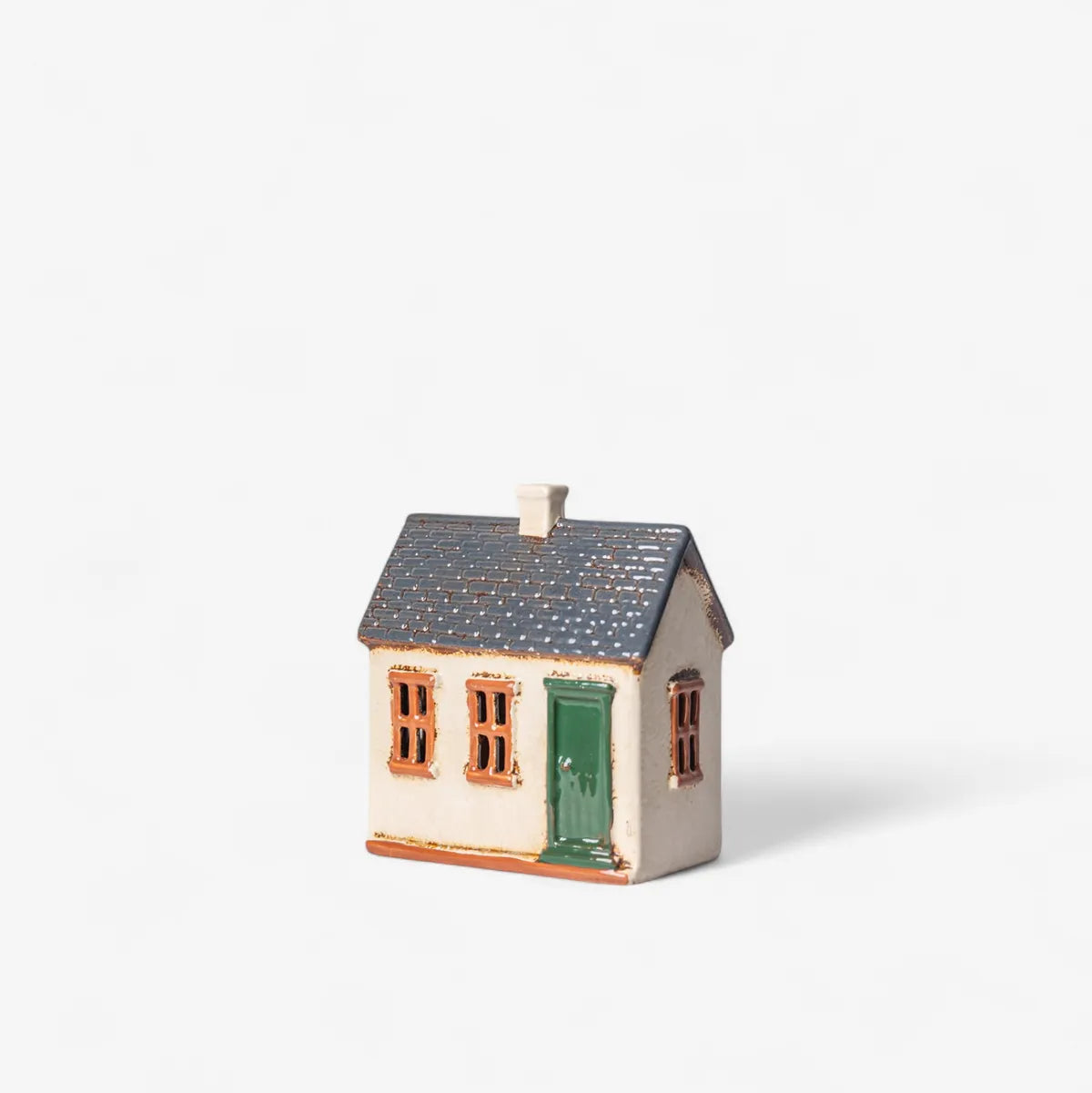 Small ceramic house with a green door on a white background