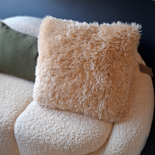 Faux fur sand coloured cushion on a textured surface with a blurred background