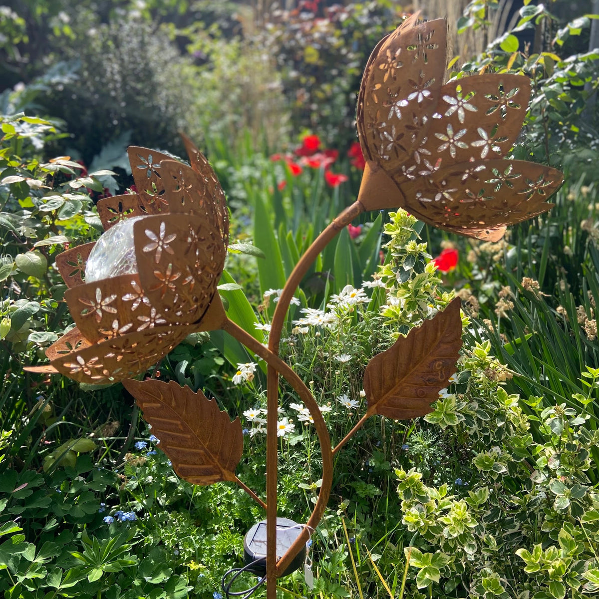 Rusty metal flower garden stake solar light
with laser-cut petal and leaf details, displayed in a lush green garden.
