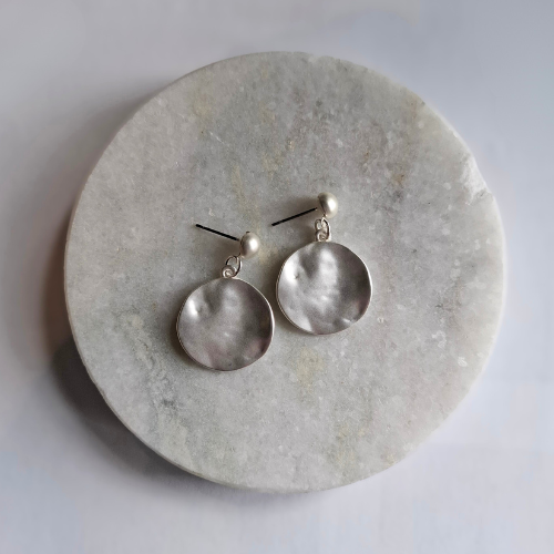 A pair of silver beaten disc earrings on a round marble surface
