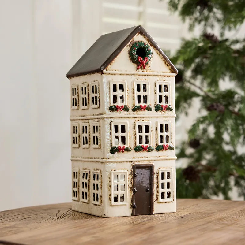 Ceramic tealight house with Christmas wreaths on a wooden surface.