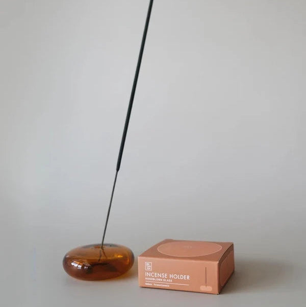 Amber incense holder with a single incense stick and its packaging on a plain background