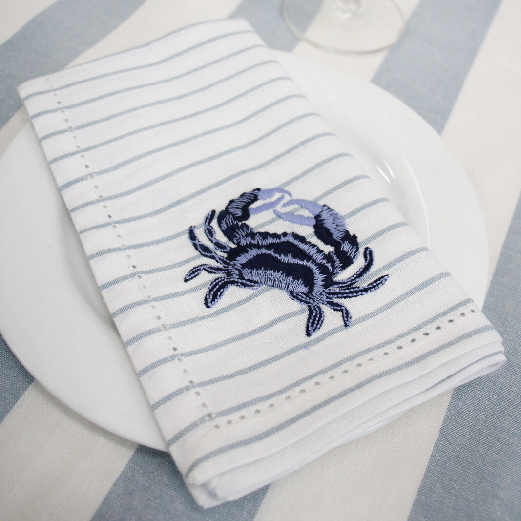 Striped napkin with a crab design on a table setting with a wine glass and flowers.