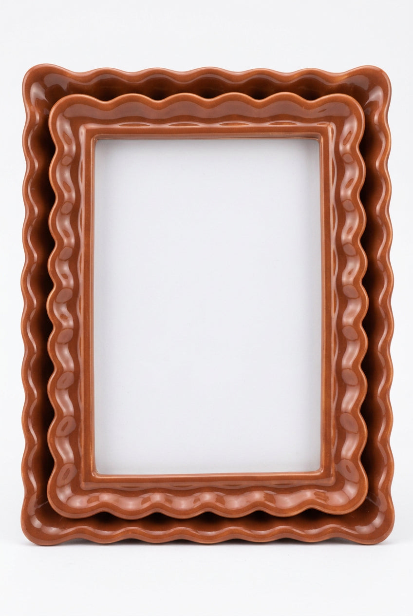 A terracotta-colored ceramic picture frame with a wavy, scalloped border