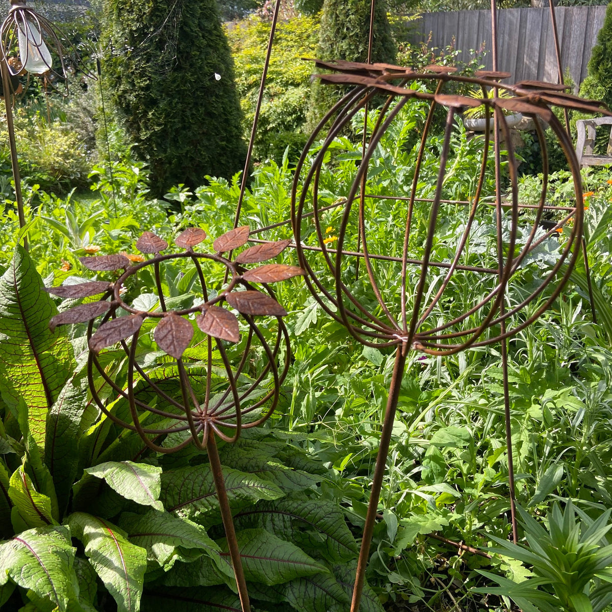 Rustic metal poppy stakes and plant supports in a lush green backyard garden.