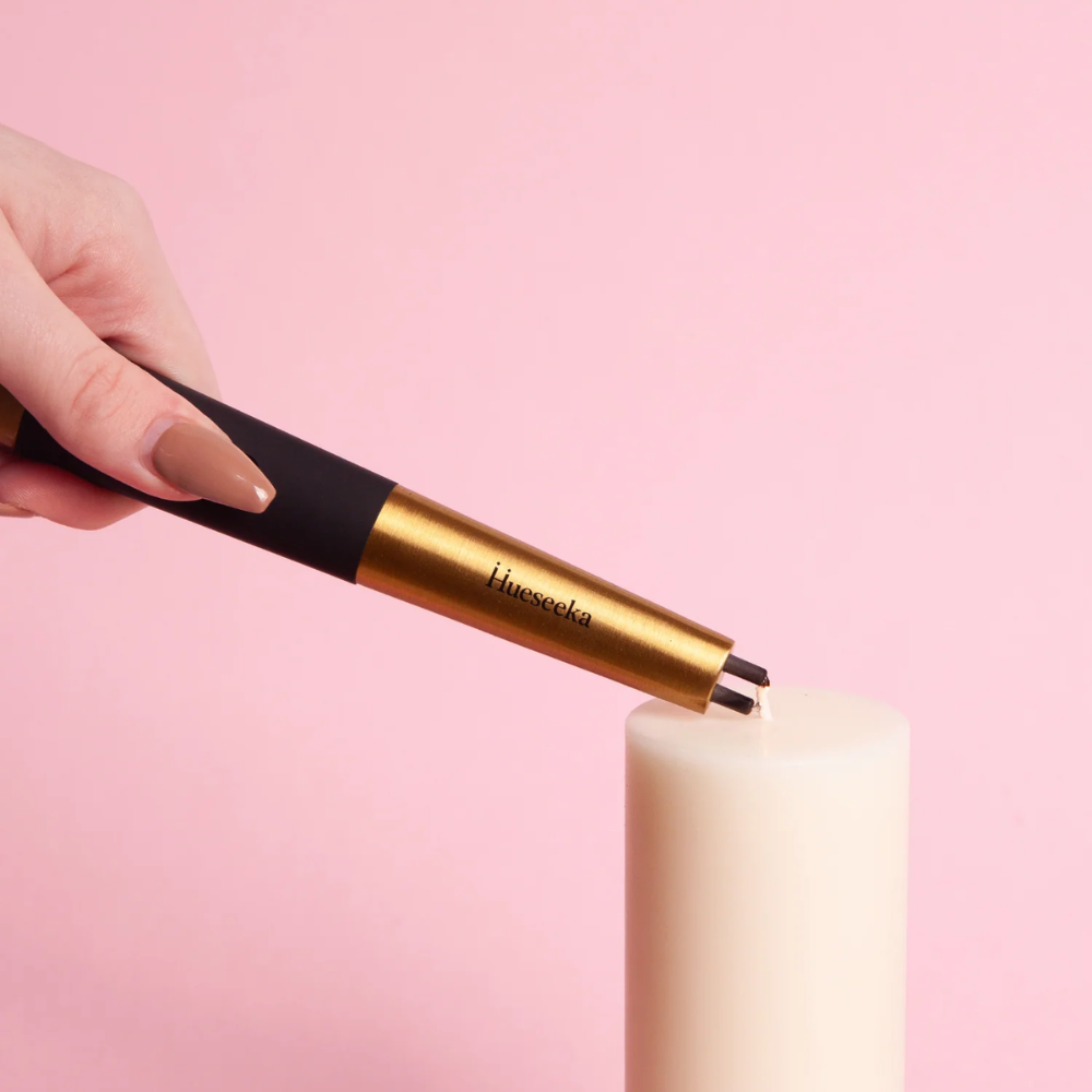 Hand holding a gold and black lighter against a pink background