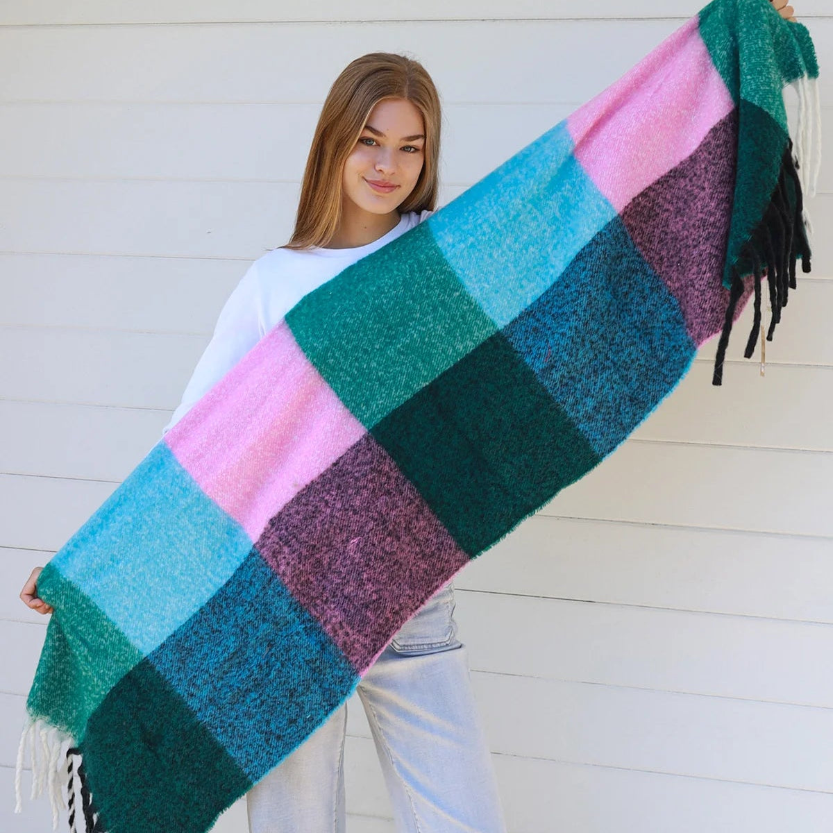 Woman holding a colorful checkered blanket against a white wall.