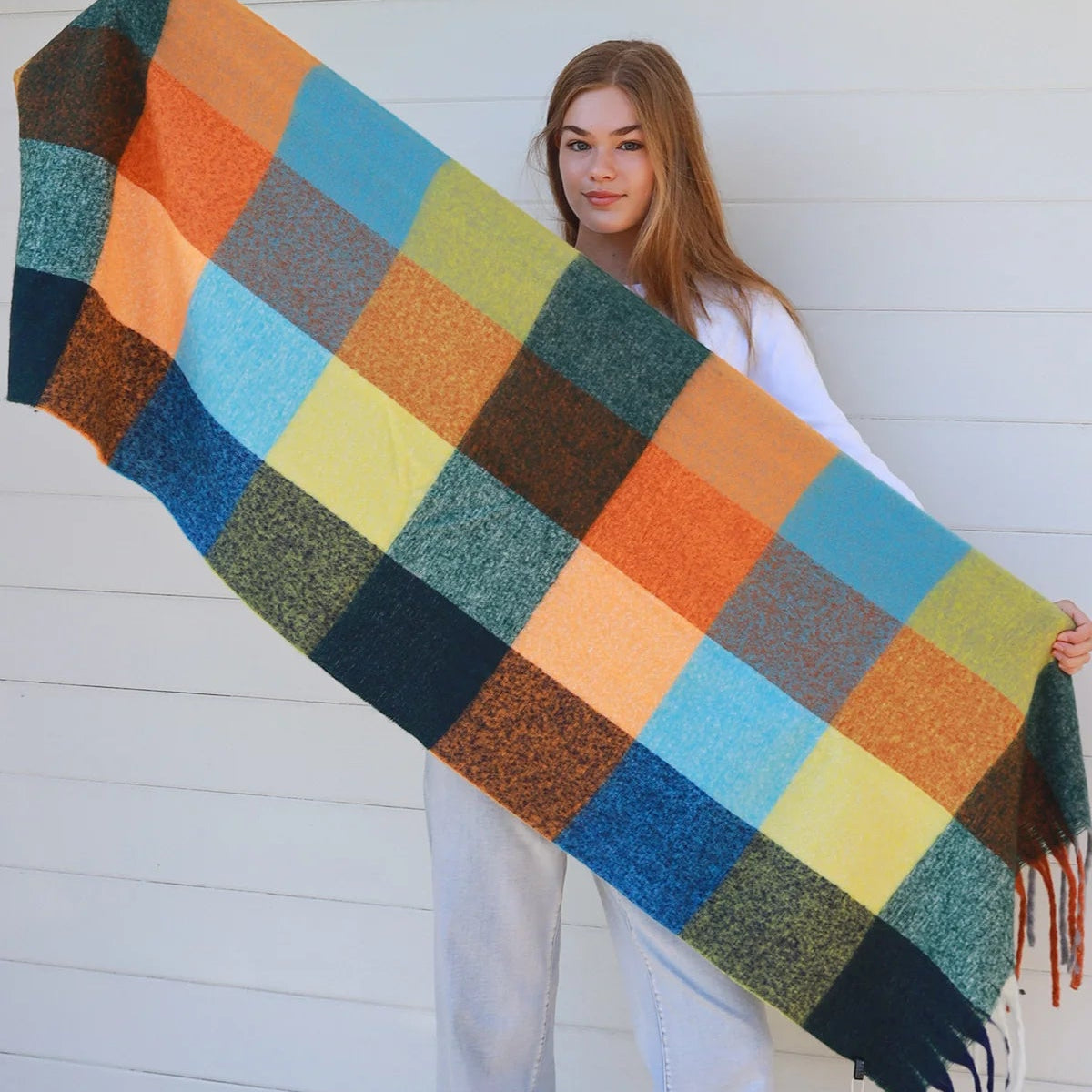 Woman holding a large, colorful checkered scarfagainst a white wall.