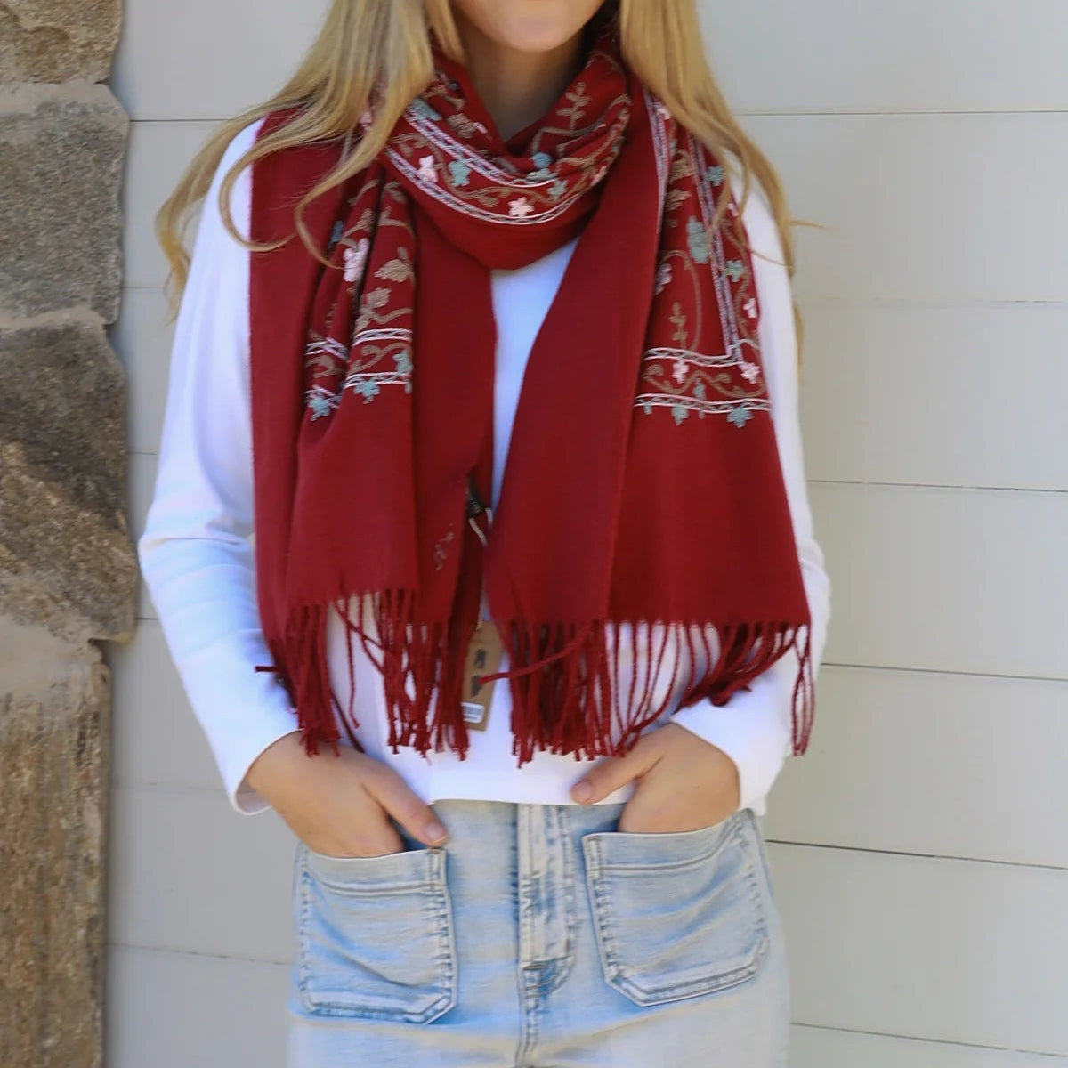 Woman wearing a red patterned scarf, white shirt, and blue jeans against a stone wall.
