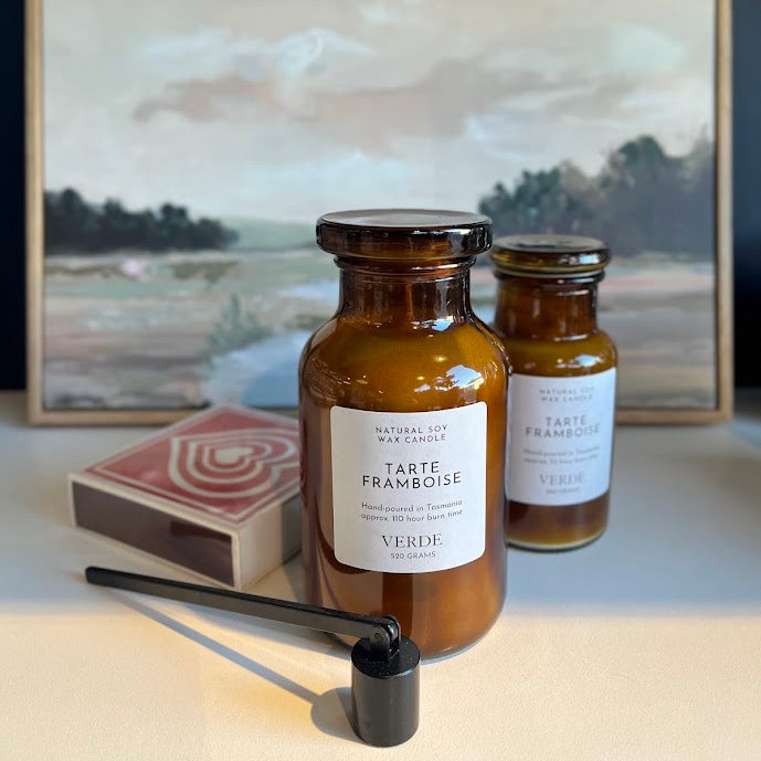 Two amber glass jars of Tarte Françoise scented tobacco with black metal lids, shown with a black pipe and a matchbox in front of a framed landscape painting.