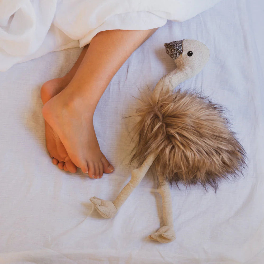 Person lying on a bed with a stuffed emu toy next to their feet.