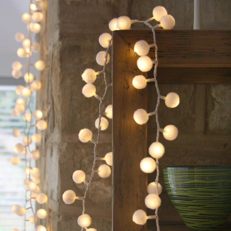 Warm white globe string lights draped over a rustic wooden shelf in a stone interior setting.