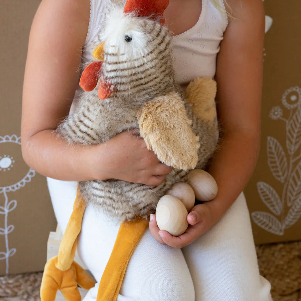 Child holding a plush rooster and eggs against a brown background