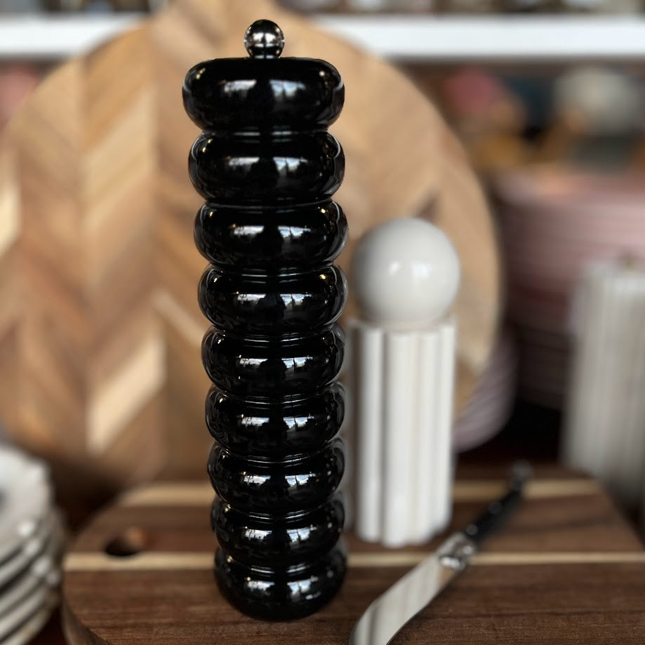 Black shiny pepper grinder on a wooden surface with blurred kitchen background