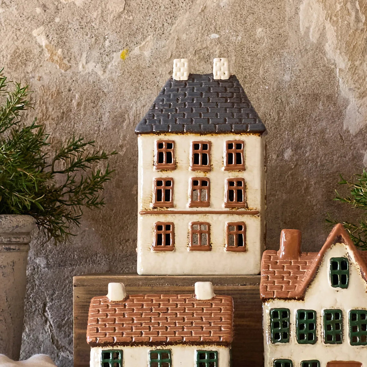 Small ceramic houses with different roof colors against a textured stone wall.
