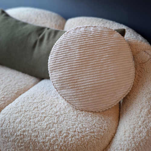 Close-up of ivory coloured corduroy round cushion on a sofa with a neutral background