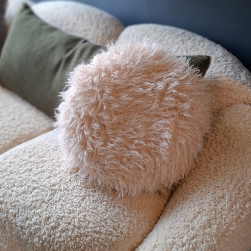 Faux fur round rose coloured cushion on a textured beige surface