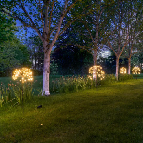 Decorative outdoor lights in a garden setting with trees and grass.