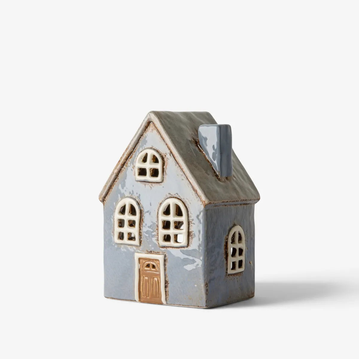 A small decorative TEA LIGHT house with a distressed blue-gray body, cream-colored arched windows, and a brown door, set against a plain light gray background.