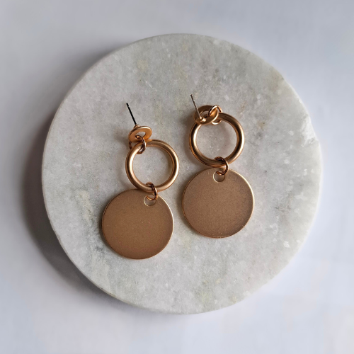 Gold hoop and disc earrings on a marble surface
