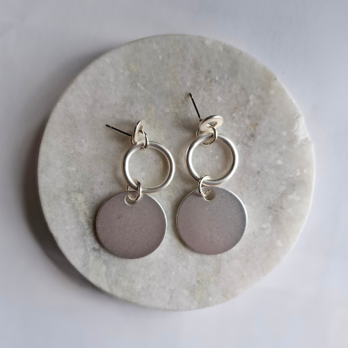 Silver hoop and disc earrings on a marble surface