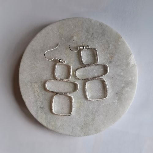 Pair of silver geo-shaped earrings on a marble surface
