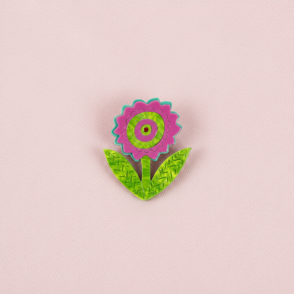 Pink flower brooch with green leaves on a white background