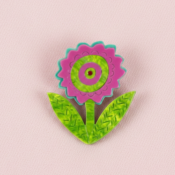 Pink flower brooch with green leaves on a white background