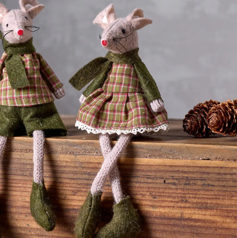 Two toy mice dressed in plaid clothing on a wooden surface with pine cones.