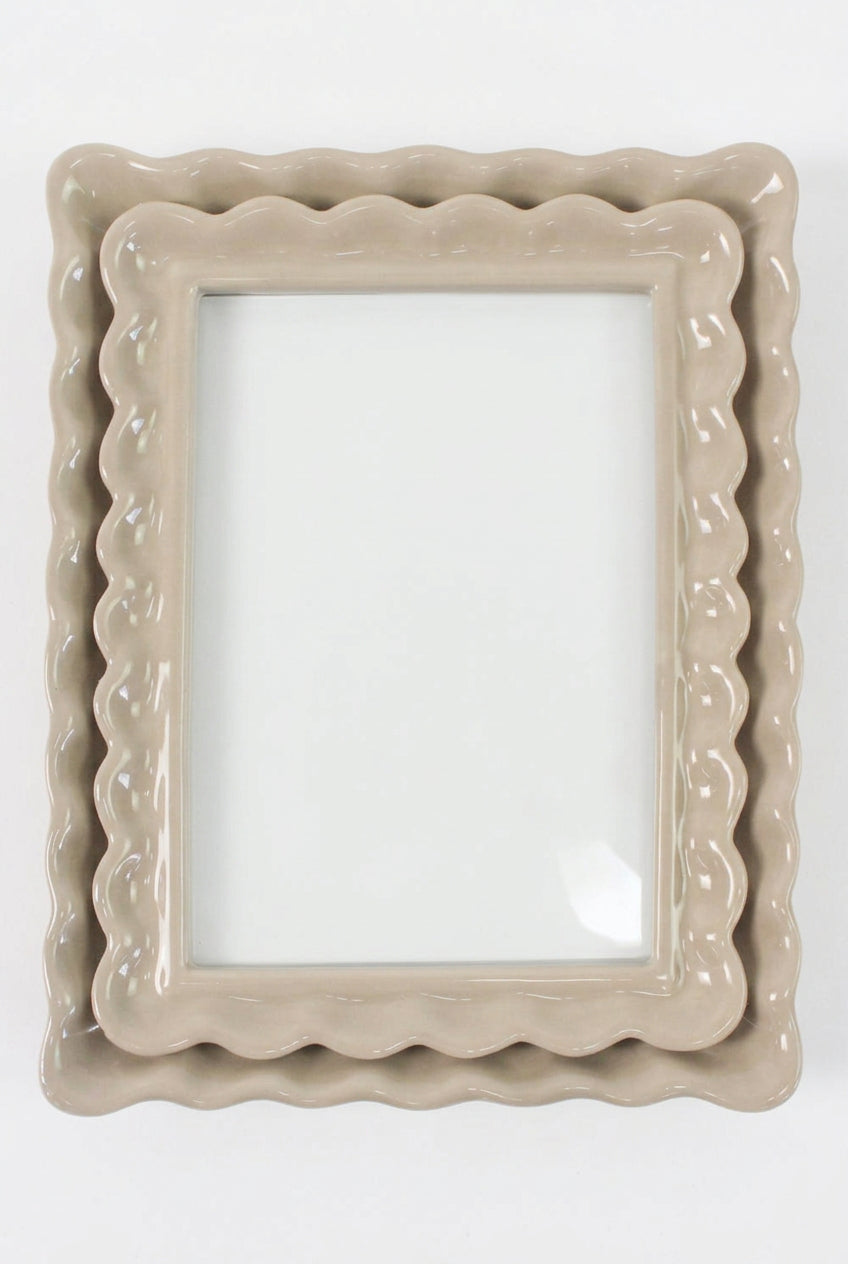 A beige ceramic photo frame with a scalloped wavy border