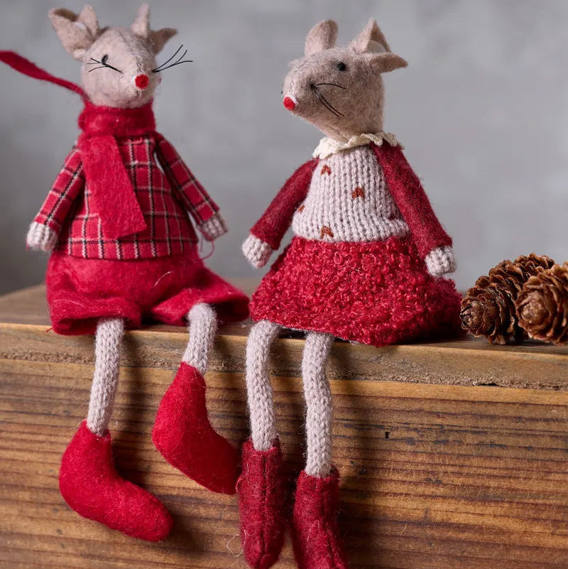 Two mouse dolls dressed in red and cream knit holiday clothing, sitting on a rustic wooden surface with pinecones against a soft gray background.