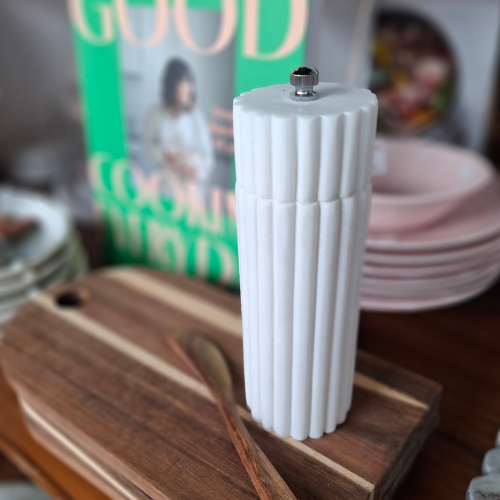 White ribbed marble salt & pepper grinder on a wooden surface with a blurred background