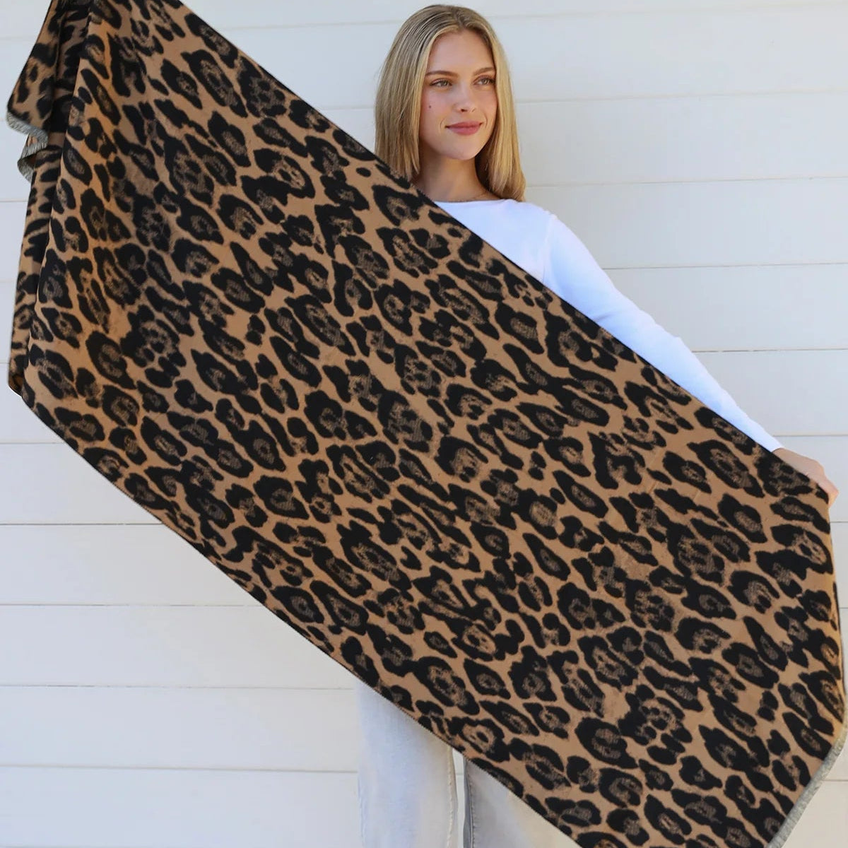 Person holding a large leopard print scarf against a white wall.