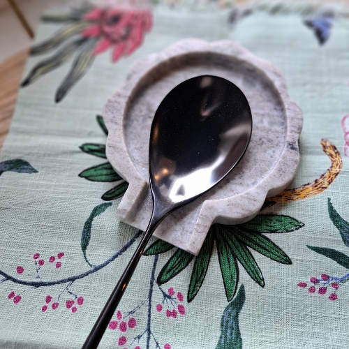 Silver spoon on a decorative marble spoon rest on a floral tablecloth