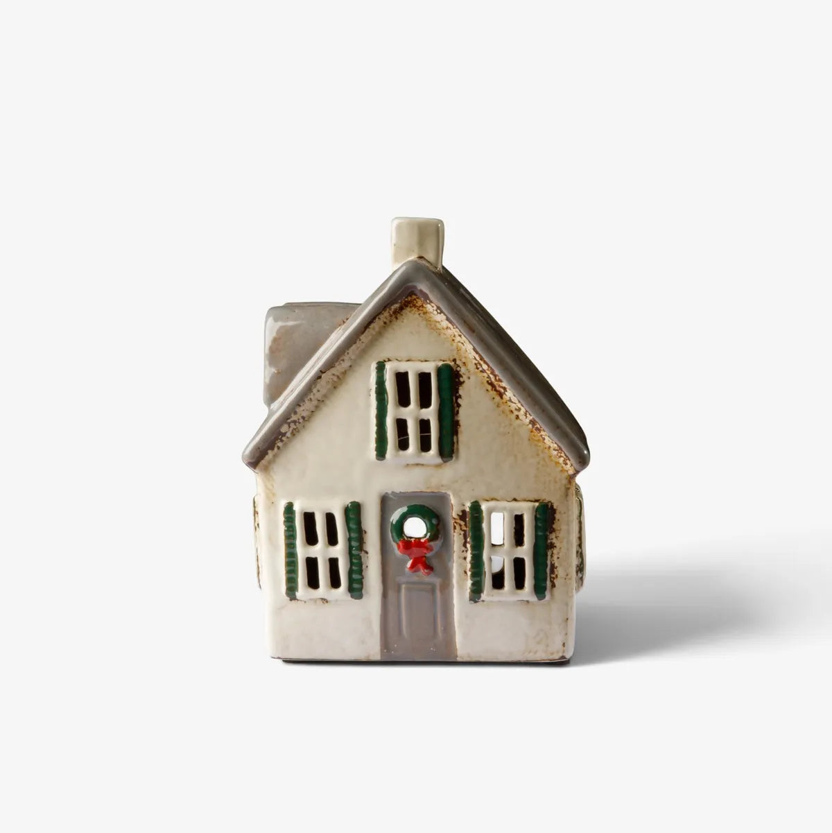 A small ceramic Christmas house figurine with a cream-colored body, dark green shutters, a gray roof, and a red bow on the front door, set against a plain white background.