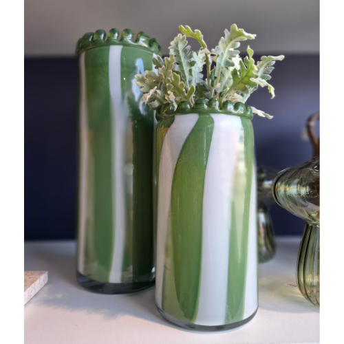 Two green and white striped vases with plants on a surface.