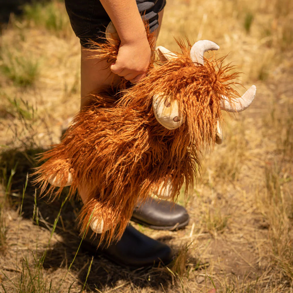 Person holding a plush toy cow in a natural setting