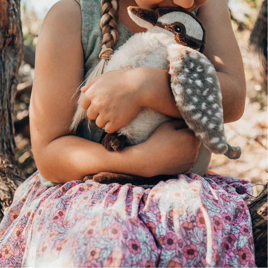 Young girl holding a kookaburra soft toy in her arms outdoors near trees