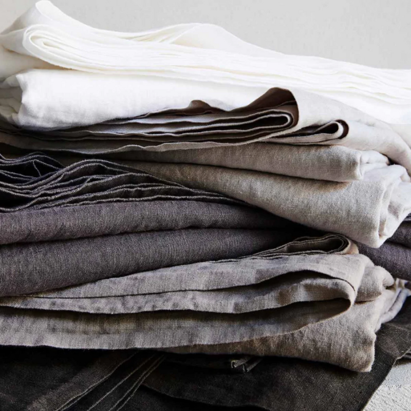 linen sheets in greys, whites, charcoal, folded and stacked in a pile